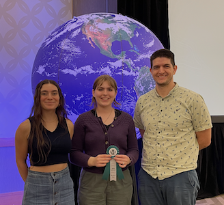 Emma, Emma, and Ben in front of a globe at the MCSR conference